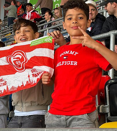 Foto: 2 Schüler halten eine Fortuna Flagge und freuen sich über ein Tor.