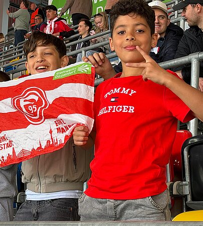 Foto: 2 Schüler halten eine Fortuna Flagge und freuen sich über ein Tor. 