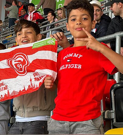 Foto: 2 Schüler halten eine Fortuna Flagge und freuen sich über ein Tor. 